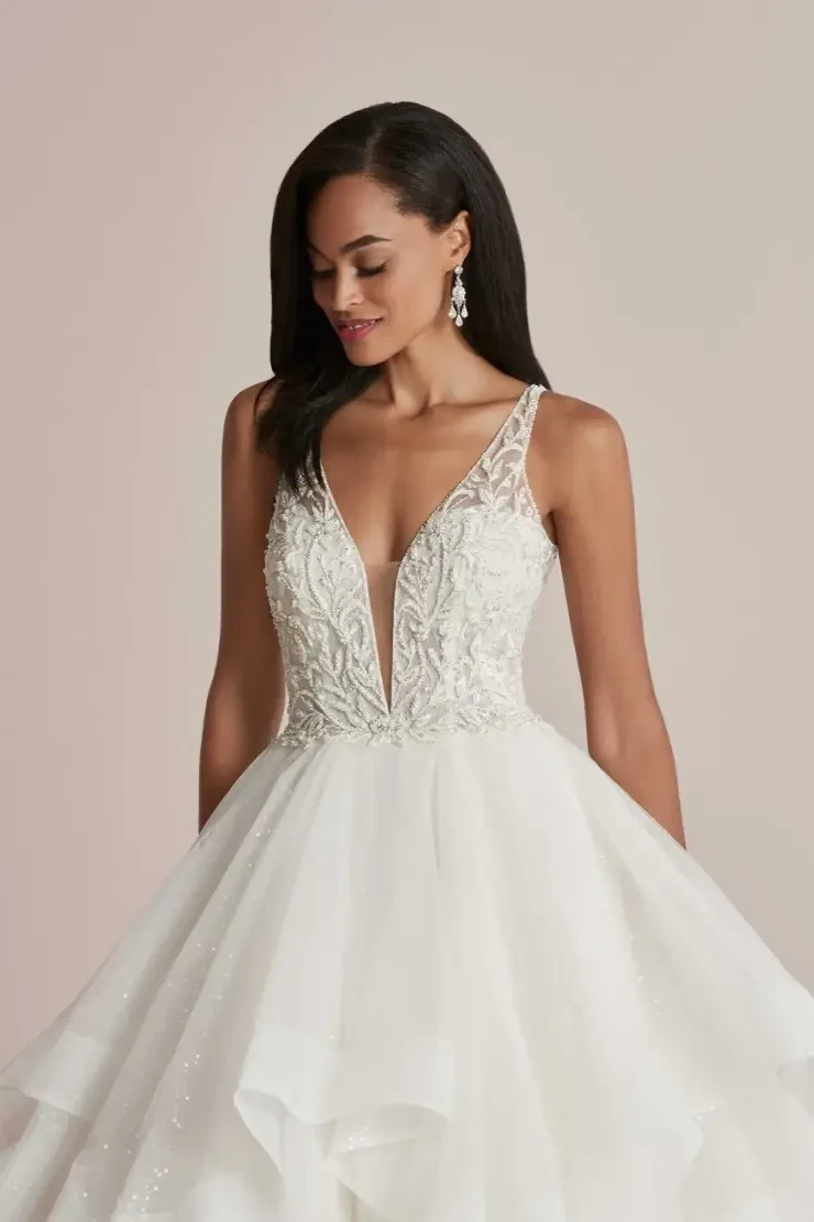 A woman wearing a beautiful bridal gown with a deep v-neckline and intricate embellishments, styled with long hair and earrings.