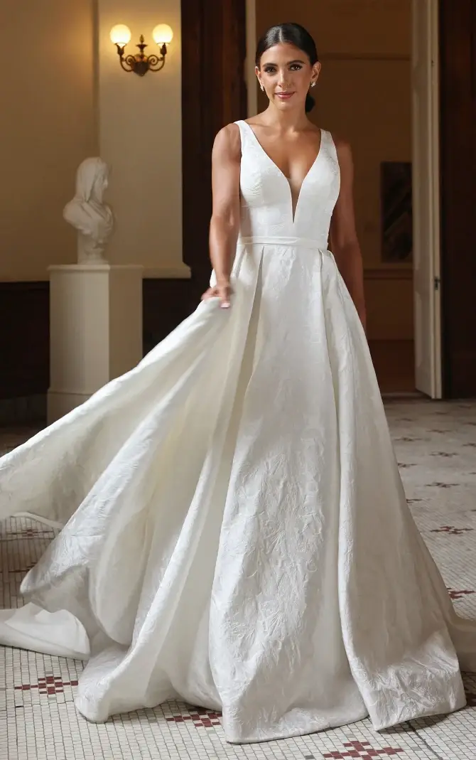 A woman in a white gown with a deep V-neckline posing in an elegant setting.