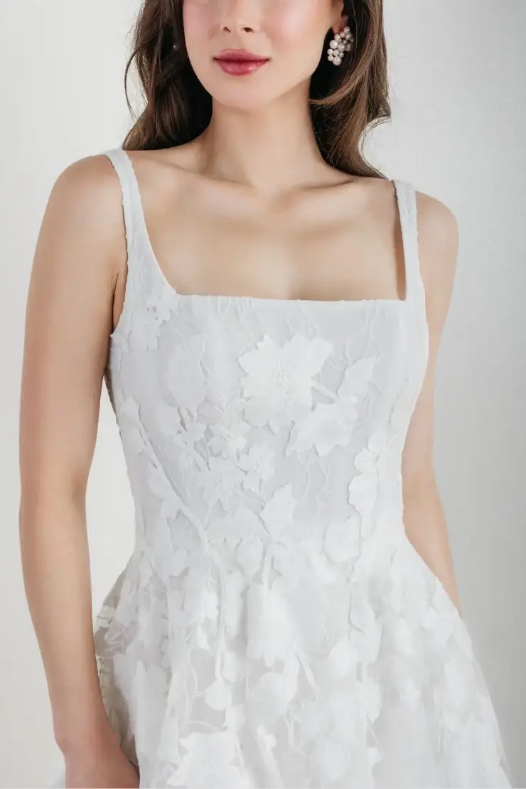 A close-up of a woman wearing a white floral dress with thin straps.
