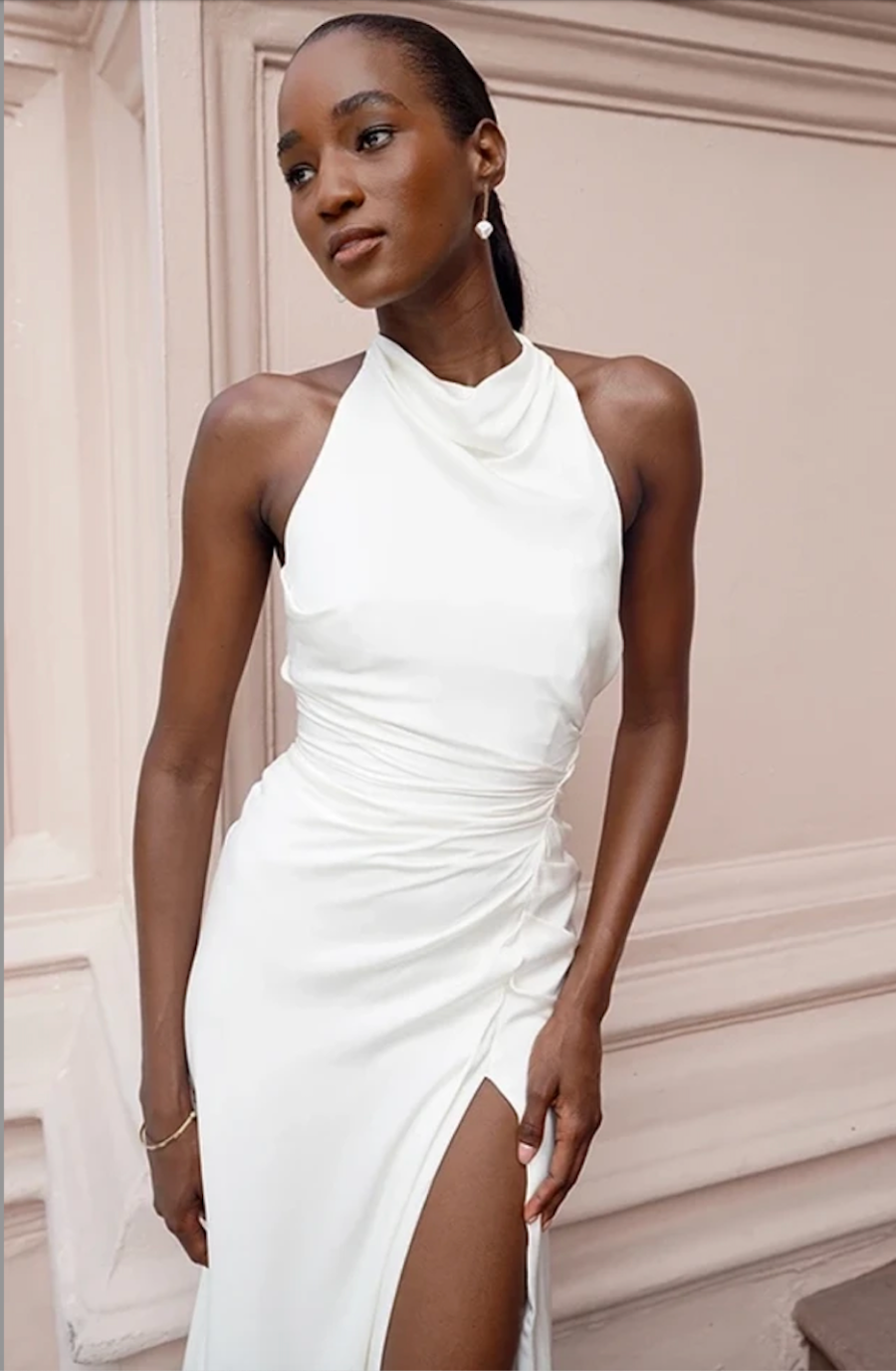 model is wearing a sleeveless high neck satin wedding dress