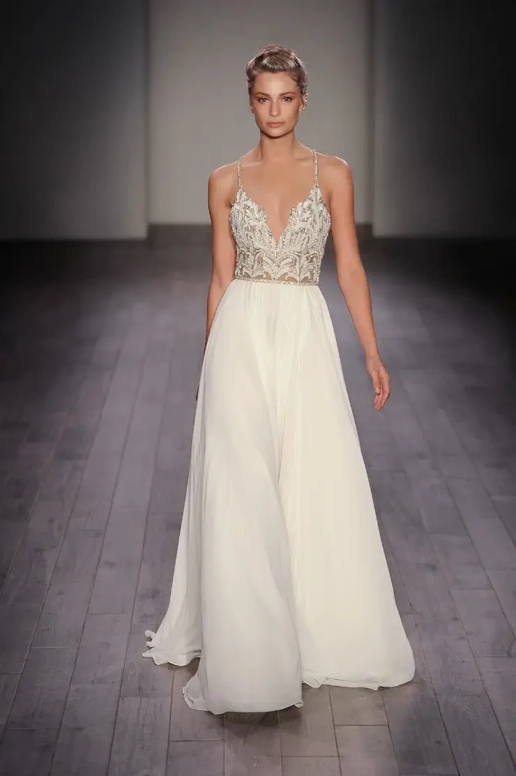 A model walking down a runway wearing a white gown with intricate detailing on the bodice.